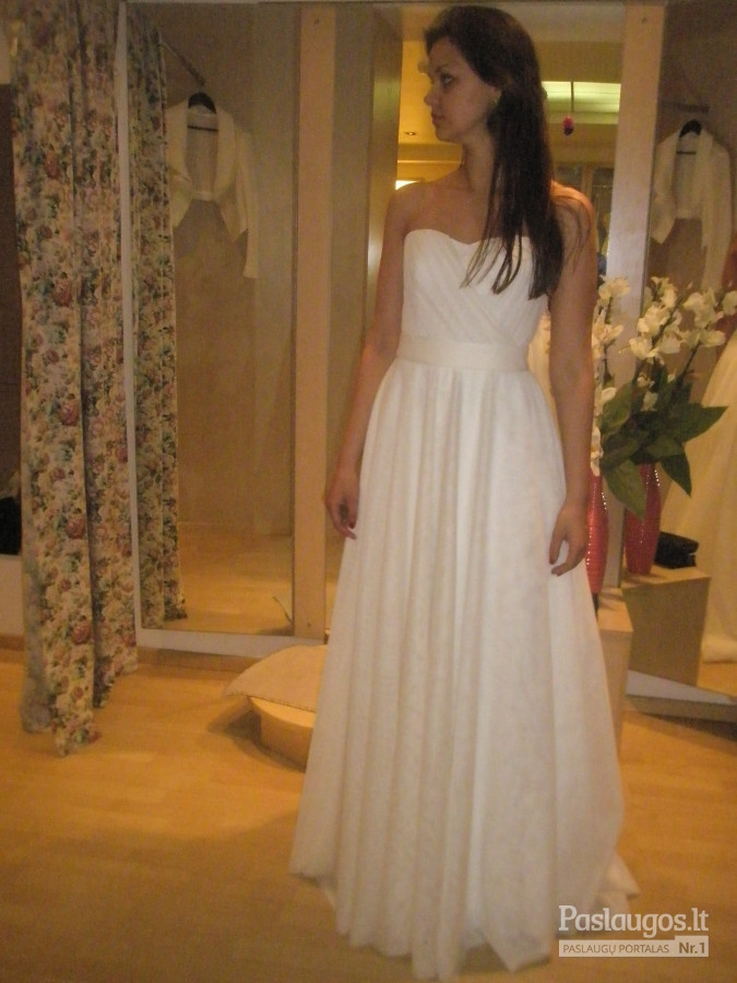 Ilga, vestuvinė suknelė. Viršus puoštas švelnia drapiruote. Apačia, platus tiulinis sijonas.