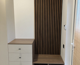 Minimalistinės linijos ir neutralios spalvos dera su medžio akcentais, sukurdamos jaukią ir tvarkingą prieskambario erdvę.