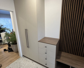 Minimalistinės linijos ir neutralios spalvos dera su medžio akcentais, sukurdamos jaukią ir tvarkingą prieskambario erdvę.