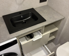 Kompaktiška skalbimo zona, kur šviesios spintelės su pilku stalviršiu suteikia didesnės erdvės pojūtį. Juodas praustuvas tampa švariu akcentu, o integruota skalbyklė ir lentynos patogiai pasiekiamos.